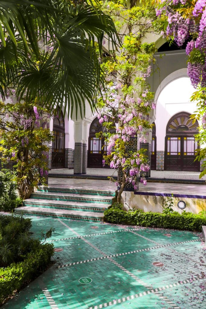 Elegant Parisian courtyard featuring lush greenery, vibrant flowers, and architectural arches, epitomizing tropical luxury.